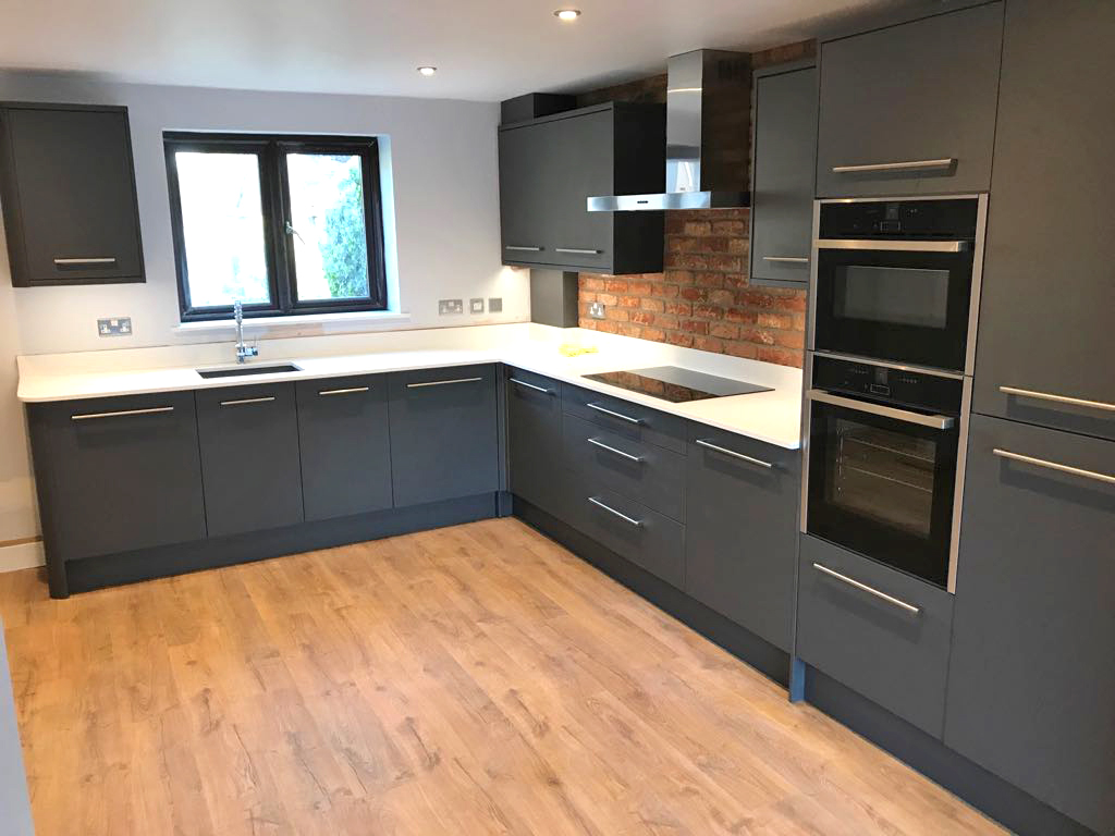 A fitted kitchen with oak flooring and a exposed brick feature wall