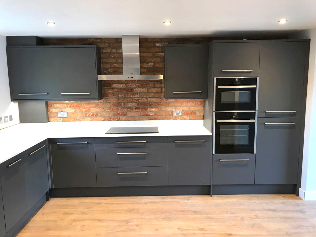 A fitted kitchen with oak flooring and a exposed brick feature wall